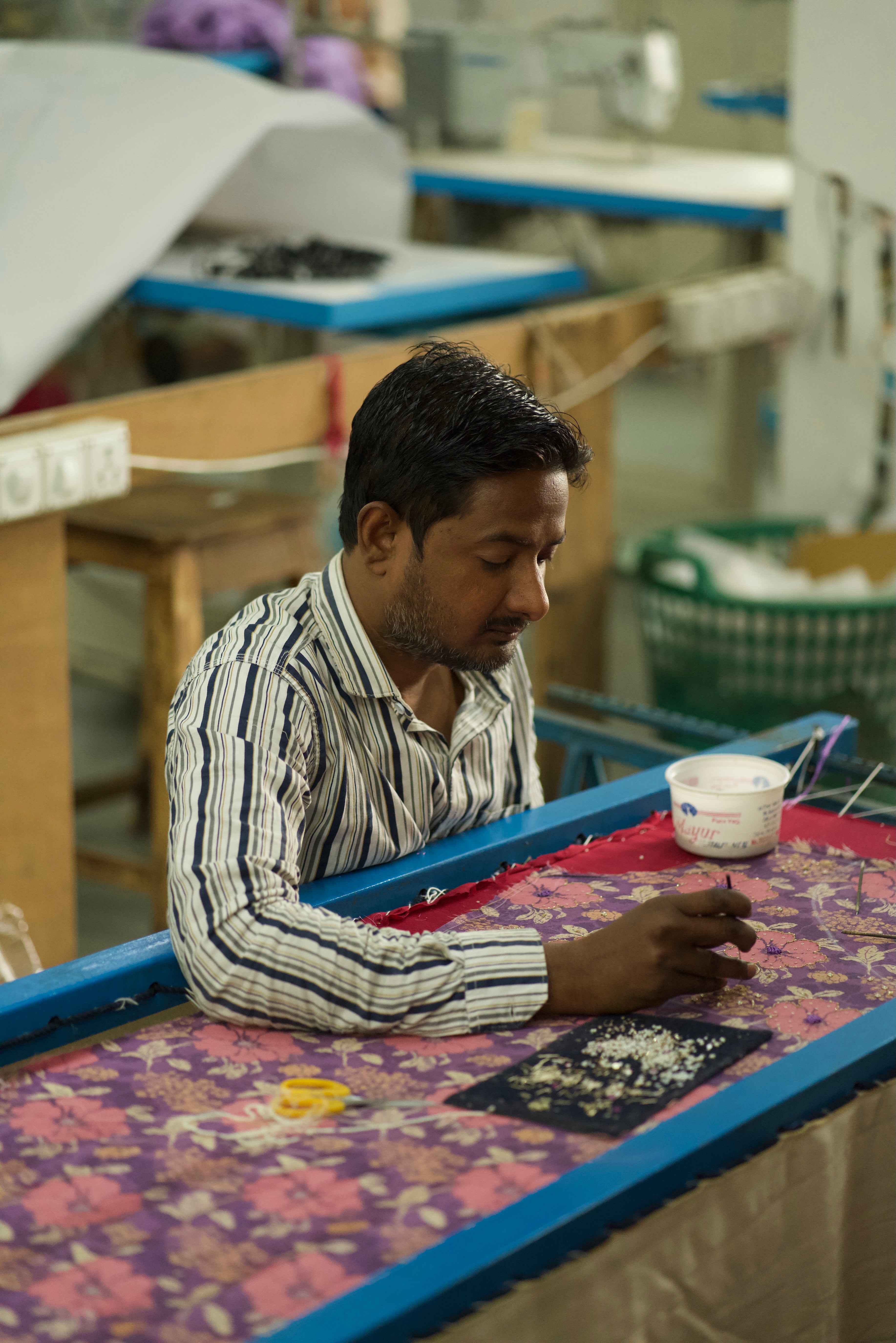 Man working at a table with a floral pattern, surrounded by equipment in a workshop setting.